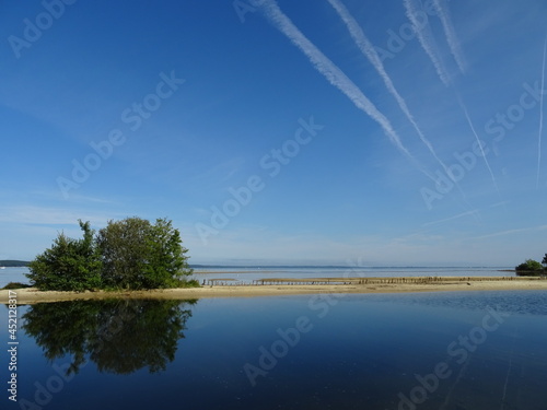 mirror reflection of trees and plane contrails in lake west france