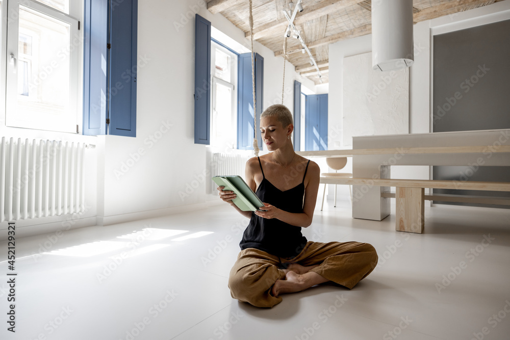Stylish woman using a digital tablet while sitting and relaxing on the floor at modern studio apartment. Digital lifestyle and leisure time at cozy home Stylish woman using a digital tablet while sitting and relaxing on the floor at modern studio apartment. Digital lifestyle and leisure time at cozy home