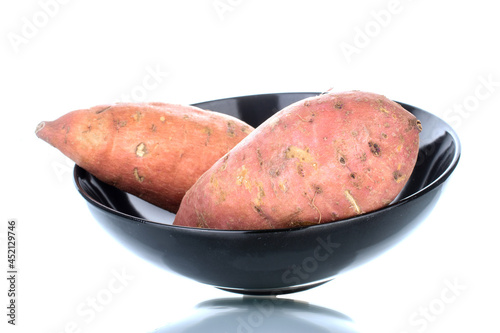 Two fresh organic sweet potatoes on a black  ceramic platter, close-up, isolated on white.