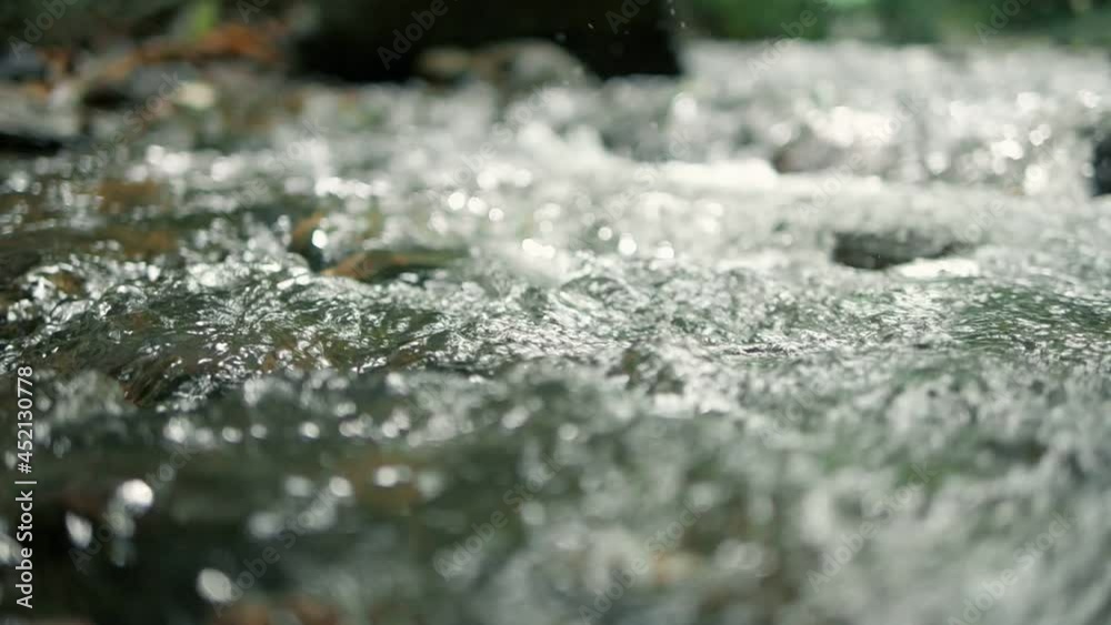 Close up slow motion of stream running fast in forest. Small waterfall with crystal clear water