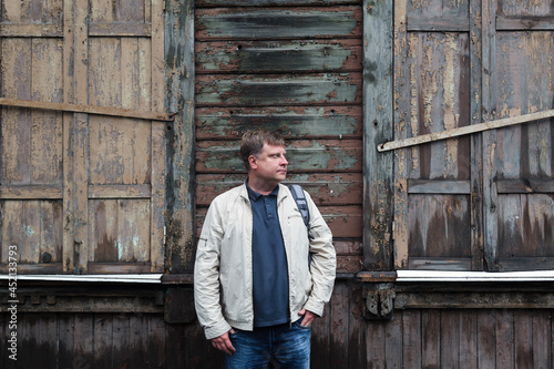 Country man farmer stands near an empty abandoned wooden building.