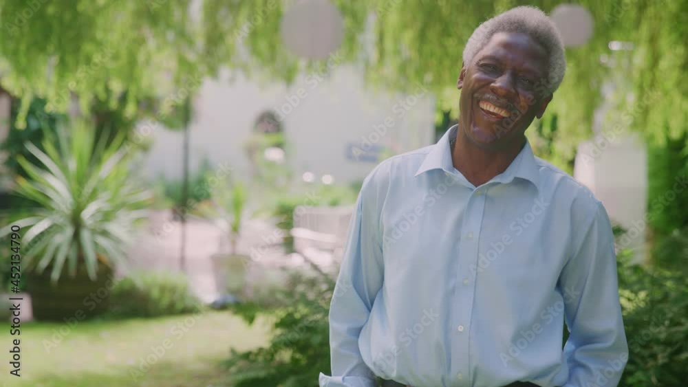 Portrait of relaxed senior man standing in garden at home after retirement smiling at camera -shot in slow motion Portrait of relaxed senior man standing in garden at home after retirement smiling at camera -shot in slow motion