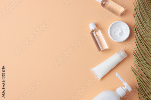Cosmetic skin care products with palm leaf on pastel beige background. Flat lay, copy space