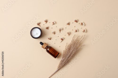 Minimal composition with cosmetic skin care products and flowers on pastel beige background. Flat lay, copy space