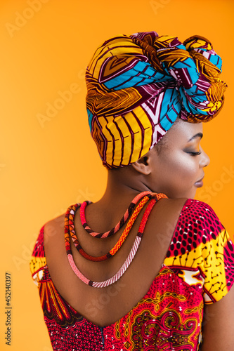Bright clothes on black leather. The African woman turned her back to the camera and dressed in national clothes.