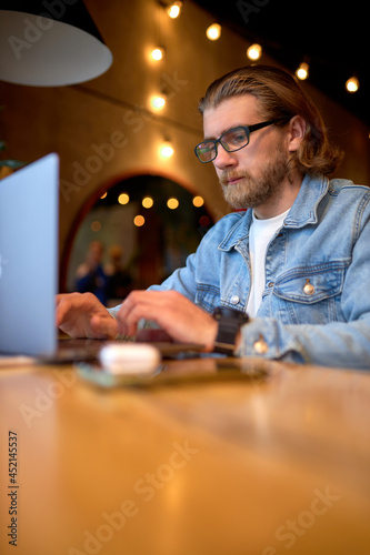 hipster lifestyle and creative workspace, caucasian guy working on laptop in coffee shop. bearded man using computer in a cafe, side view shot. copy space. focus on male looking at screen of laptop