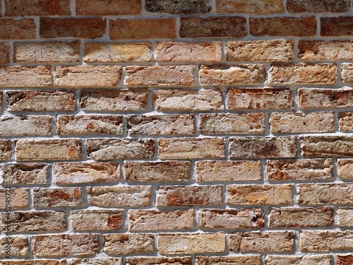 uneven brickwork in sunlight, exterior surface made of sandy-orange bricks with space for text, textured brick background with irregularities, cracks and decay photo