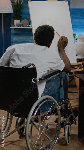 Black young artist with handicap drawing vase on canvas and easel at studio. African american creative man in wheelchair designing modern masterpiece for authentic fine art project