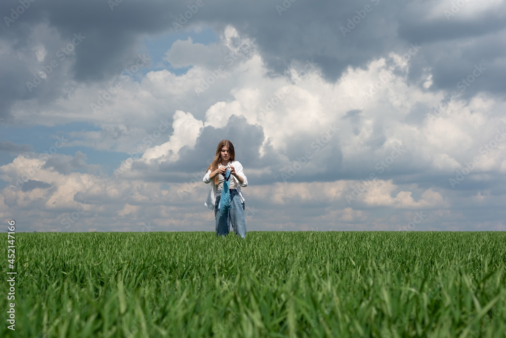 little teenager girl running in a field of green grass, against the backdrop of a cloudy sky