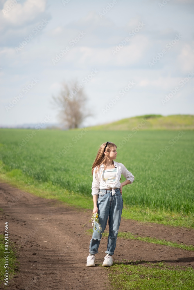 fashionable little girl in a field on a path, against a background of clouds
