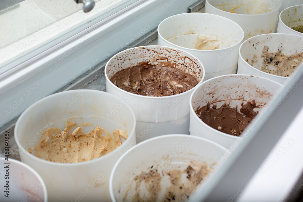 A view looking into a cold storage display at a local ice cream shop, featuring a variety of flavors inside plastic containers.