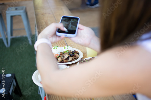 A view of a woman taking photos of food with her cell phone, in an outside patio setting.