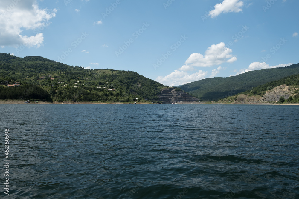 Beautiful Zavojsko jezero (Zavoj lake) view over the wavy water with sunlit mountains and green forests on the other side and rafts in the water