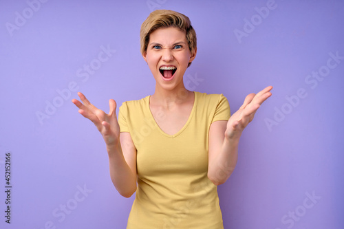 caucasian woman scream isolated in studio on purple background, young female is spreading arms, irritated by something, angry lady in casual tshirt expressing dissatisfaction, portrait copy space © alfa27