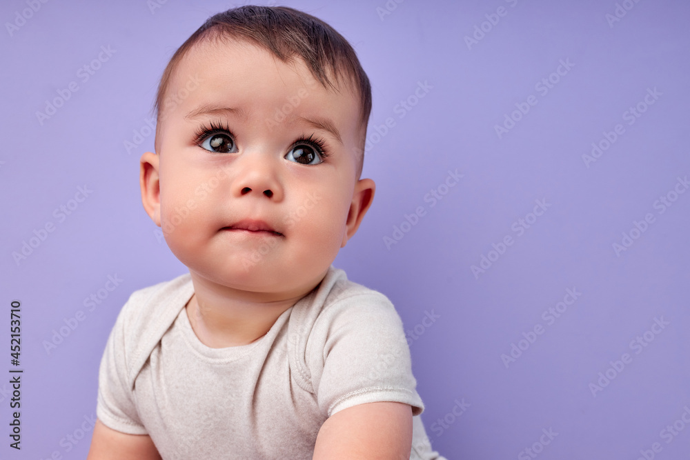 Sweet baby girl is going to cry, looking very cute, isolated on purple studio background. Beautiful Caucasian child in casual wear looking at side. Copy space. Children, childhood concept