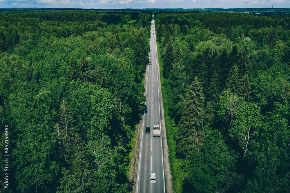 Aerial drone view of green forest with country road.