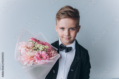 Cute adorable boy in suit with bouquet of fresh flowers. Little cheerful gentelman photo
