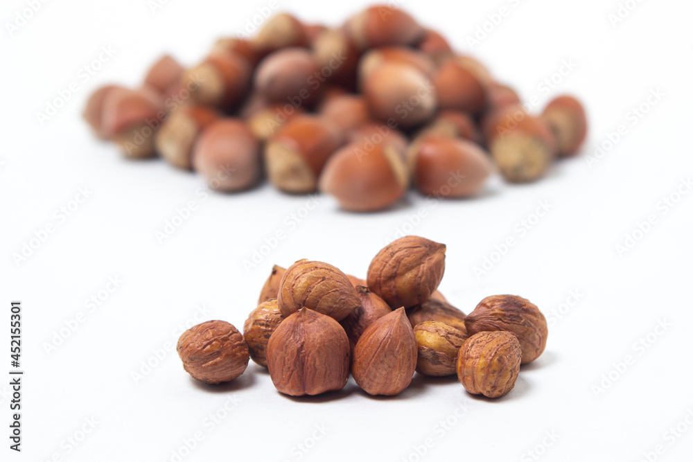 Peeled hazelnuts next to a whole hazelnut on a white background. Healthy diet Peeled hazelnuts next to a whole hazelnut on a white background. Healthy diet
