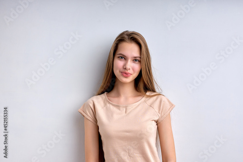 Portrait of shy caucasian teenage girl isolated on white background, smiling happily, in casual wear, enjoying life, in good mood, posing at camera, having natural long hair and big lips.