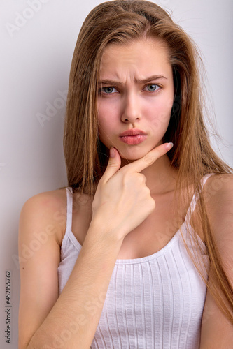 close-up portrait of dissatisfied pretty woman with natural straight hair is looking outraged, wearing casual clothes having displeased look posing in studio against white background, touching chin