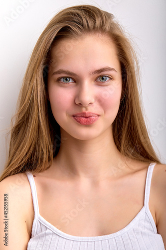 Delighted caucasian female in white undershirt looking at camera happily  isolated on white studio background  copy space. Satisfied girl with natural long hair posing  indoors. human emotions concept