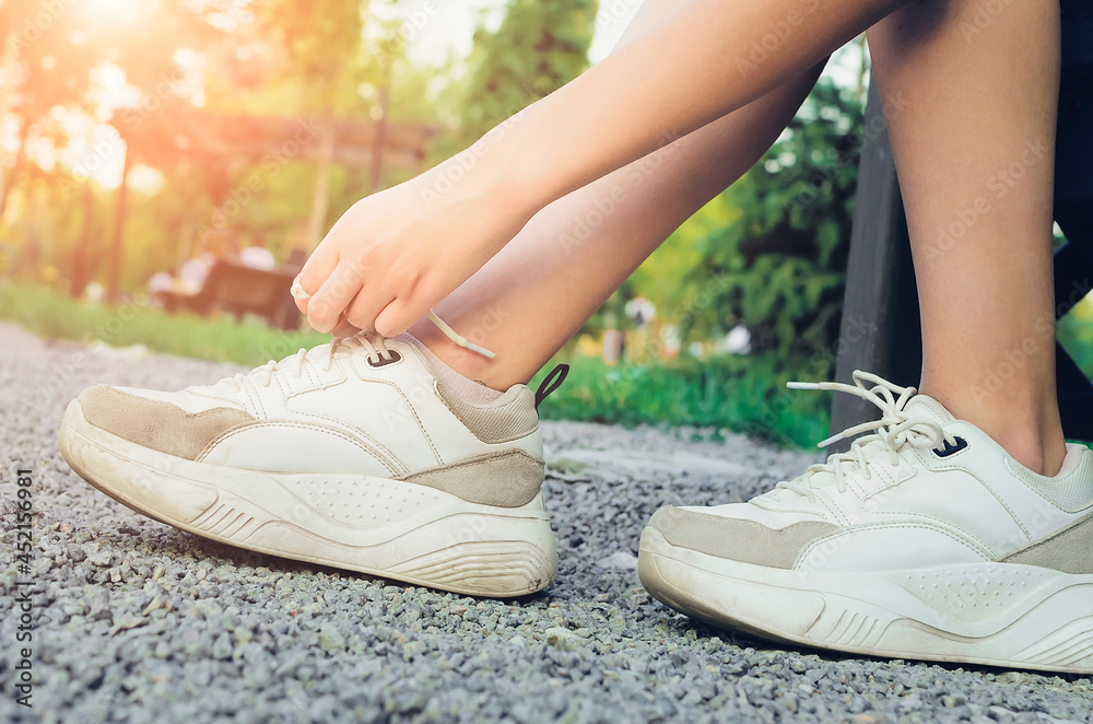 Naklejka premium Girl tying laces on sneakers on the street, close-up. Sport active lifestyle concept. Close-up