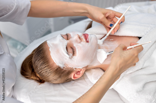 Young cropped woman cosmetologist apply white clay mask on woman's face. Beautiful caucasian client woman in beauty salon get spa procedures, cleansing face. natural beauty, cosmetology concept