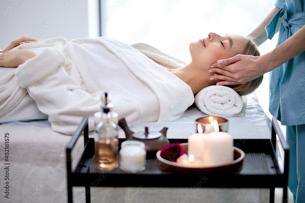 Young woman doing relaxing face massage in salon. Classic massage for purpose prevention. Anxiety disappears, tension is relieved. Lady in cozy atmosphere cabin to feel peace and quiet, side view Young woman doing relaxing face massage in salon. Classic massage for purpose prevention. Anxiety disappears, tension is relieved. Lady in cozy atmosphere cabin to feel peace and quiet, side view
