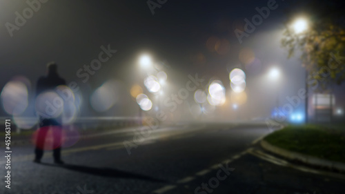 A mysterious figure standing in the middle of the road on a misty night. With a blurred, bokeh, out of focus edit