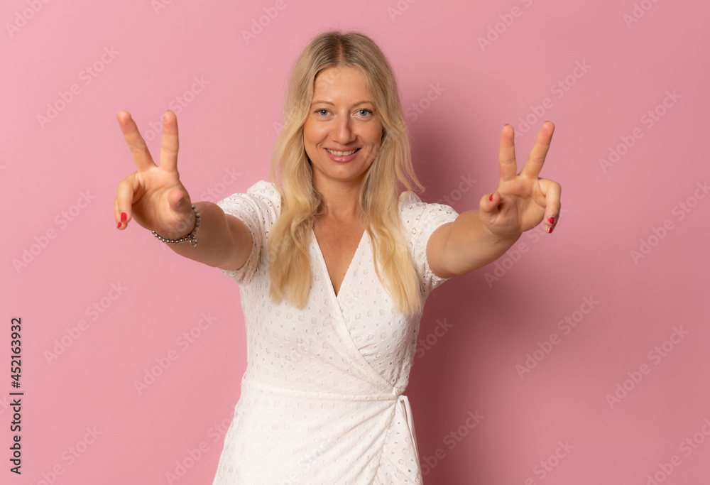 Young blonde woman in casual dress showing victory sign isolated over pink background. Young blonde woman in casual dress showing victory sign isolated over pink background.