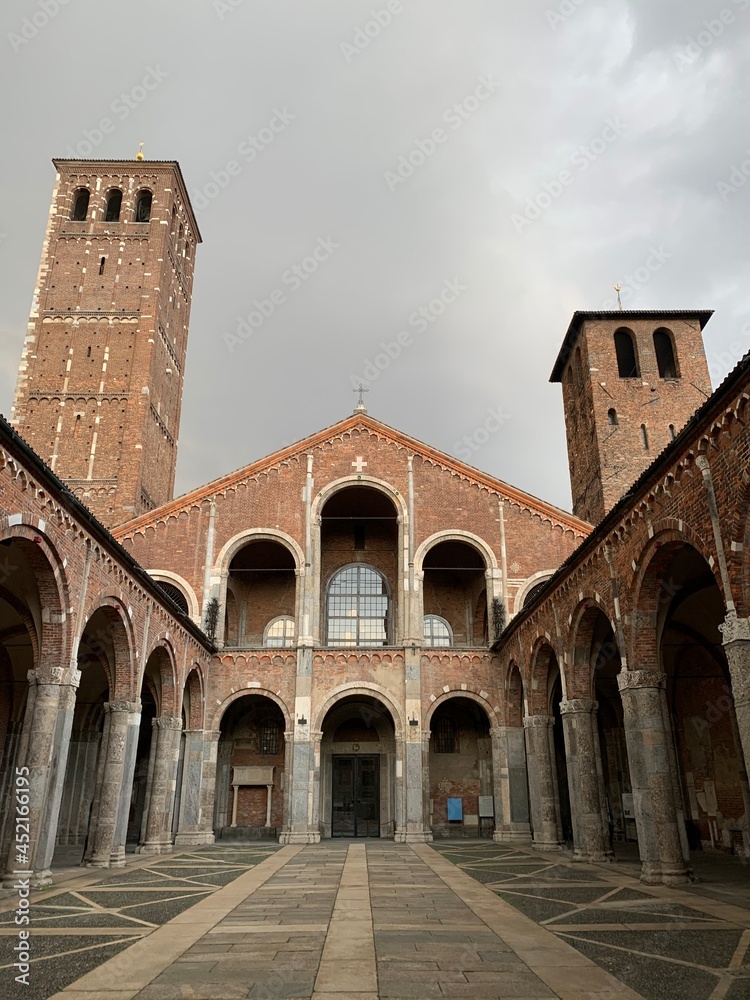 Facade of the Basilica di Sant'Ambrogio. Courtyard of ancient Romanesque style church. Bell towers on the sides. Milan, Lombardy, Italia.