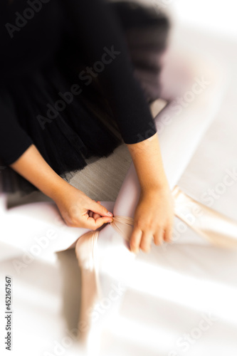 Legs and black fluffy skirt of little balerina wearing pail pink pointe shoes with ribbons