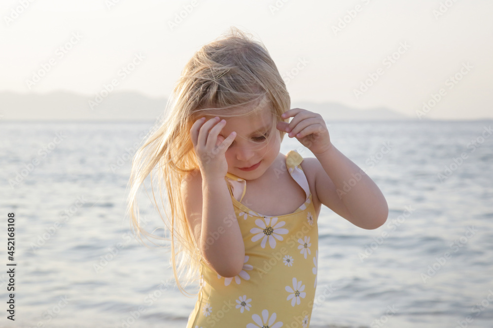 Adorable toddler girl in yellow swimsuit enjoying a day at the beach. Idyllic summer vacation. Adorable toddler girl in yellow swimsuit enjoying a day at the beach. Idyllic summer vacation.
