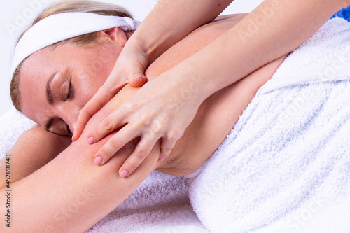 Close up photo of a woman being in a spa salon lying on the massage table with her hands under her head with closing eyes  undergoes a shoulder massage.