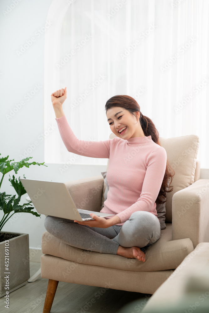 Beautiful of portrait asian young woman excited and glad of success with laptop on sofa Beautiful of portrait asian young woman excited and glad of success with laptop on sofa