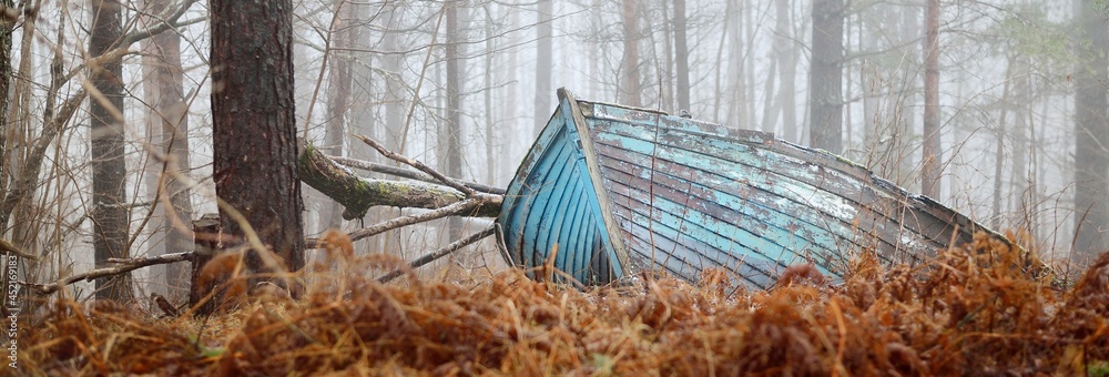 Abandoned old blue wooden boat in a mysterious winter forest. Mossy trees in a white mist. Fresh snow and golden autumn leaves. Concept art, economic decline, recession, philosophy, contrasts, paradox - obrazy, fototapety, plakaty 