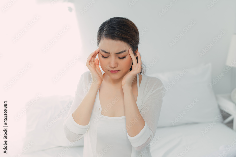 Miserable young woman touching temples sitting on bed at home, Miserable young woman touching temples sitting on bed at home,