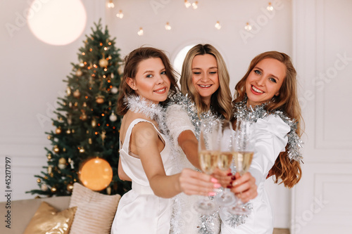 Beautiful young women girlfriends in elegant dresses have fun together laugh drink and celebrate the new year at a party in a cozy house during the Christmas holidays, selective focus