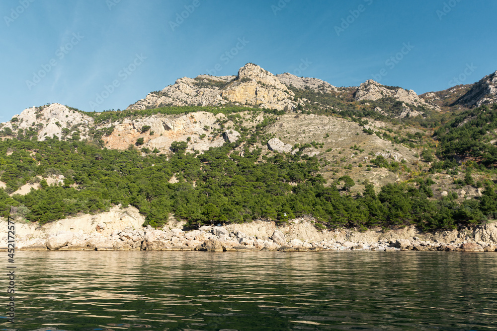 Sea mountains forest summer green landscape. Beautiful pine trees against the background of gray rocks of the blue sky. A secluded place to travel. Colorful beaches near Balaklava. Wild beaches Crimea