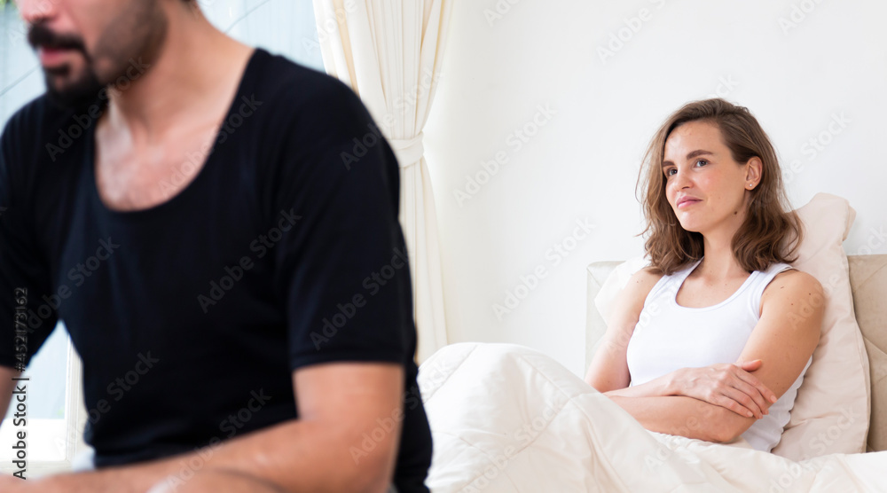 Selected focus on young upset female sitting on bed, her boyfriend sitting on the edge of the bed. They are having family problems. Unhappy couple having problems at bedroom. Selected focus on young upset female sitting on bed, her boyfriend sitting on the edge of the bed. They are having family problems. Unhappy couple having problems at bedroom.