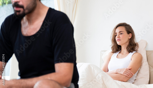 Selected focus on young upset female sitting on bed, her boyfriend sitting on the edge of the bed. They are having family problems. Unhappy couple having problems at bedroom.