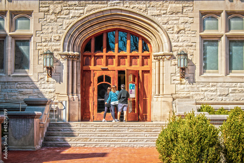Parents and female student entering large arched doors of University building flanked by metal gothic lamps.