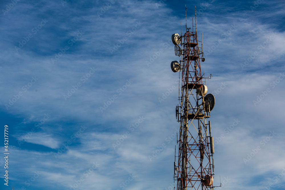 Telecommunication pole with several kinds of antennas in blue sky and clouds in sunny bright day with copy space
