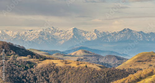 Panoramic landscape view over Gum-bashi mountain pass, with new green and old brown grass on cliffs, dark clouds before the storm, Сaucasus mountian range and Elbrus mountain. Karachay-Cherkessia