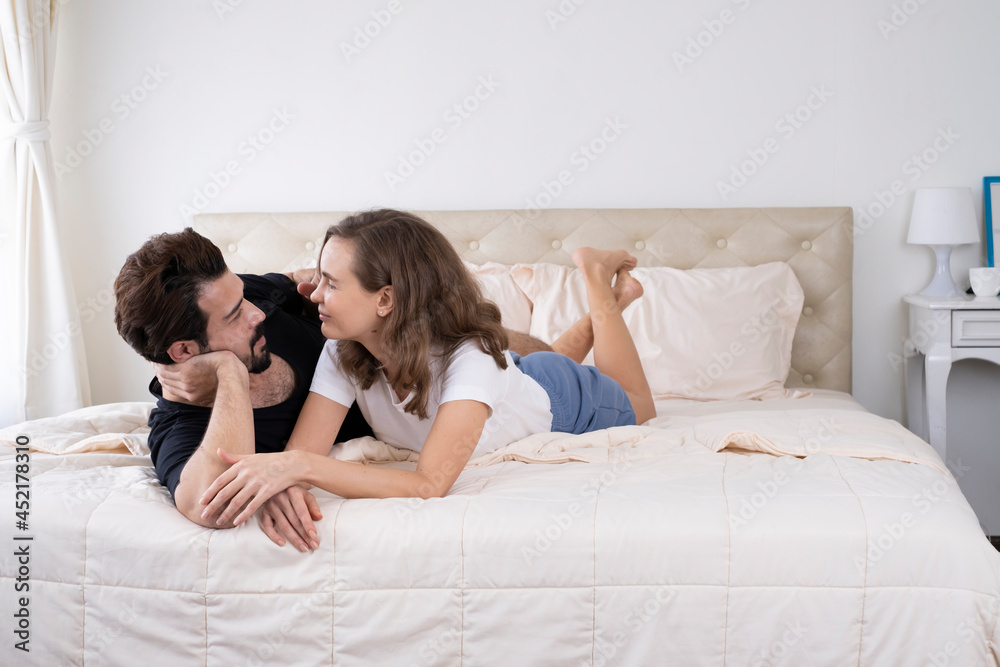 Happy couple relaxing in bed and holding hands and talking in the morning. Young loving couple in the bed. Happy young couple lying together in bed. Happy couple relaxing in bed and holding hands and talking in the morning. Young loving couple in the bed. Happy young couple lying together in bed.