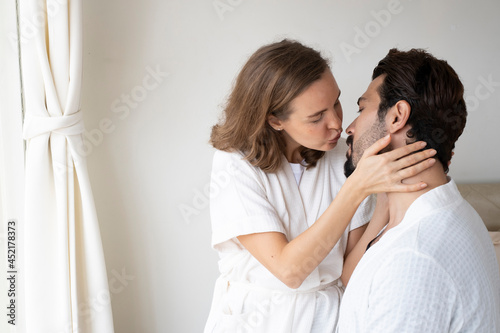 Couple wearing bathrobe on bed kissing eachother. Husband and wife wearing bathrobe sitting together on the bed. Happy couple in bathrobes sitting on bed at home.