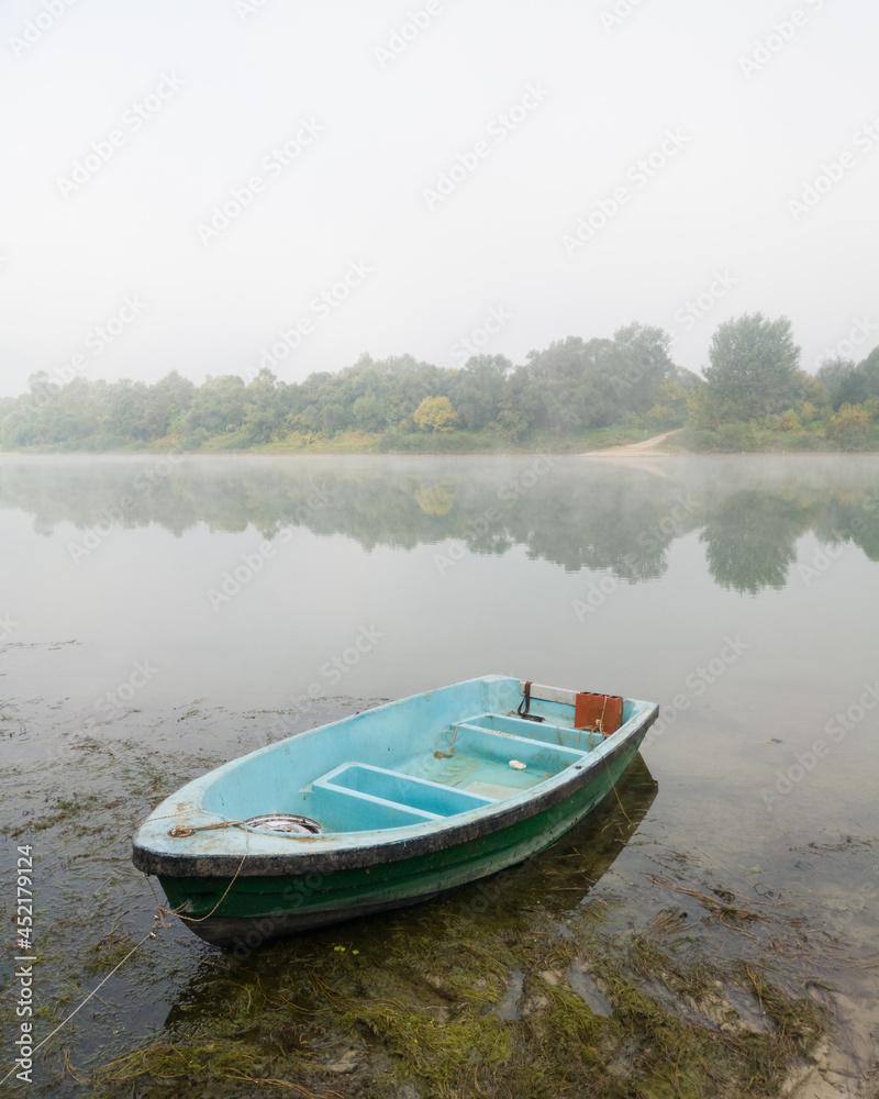 Landscape of Sava river in autumn, moored green and blue boat in shallow water surrounded with algae during beautiful misty morning Landscape of Sava river in autumn, moored green and blue boat in shallow water surrounded with algae during beautiful misty morning