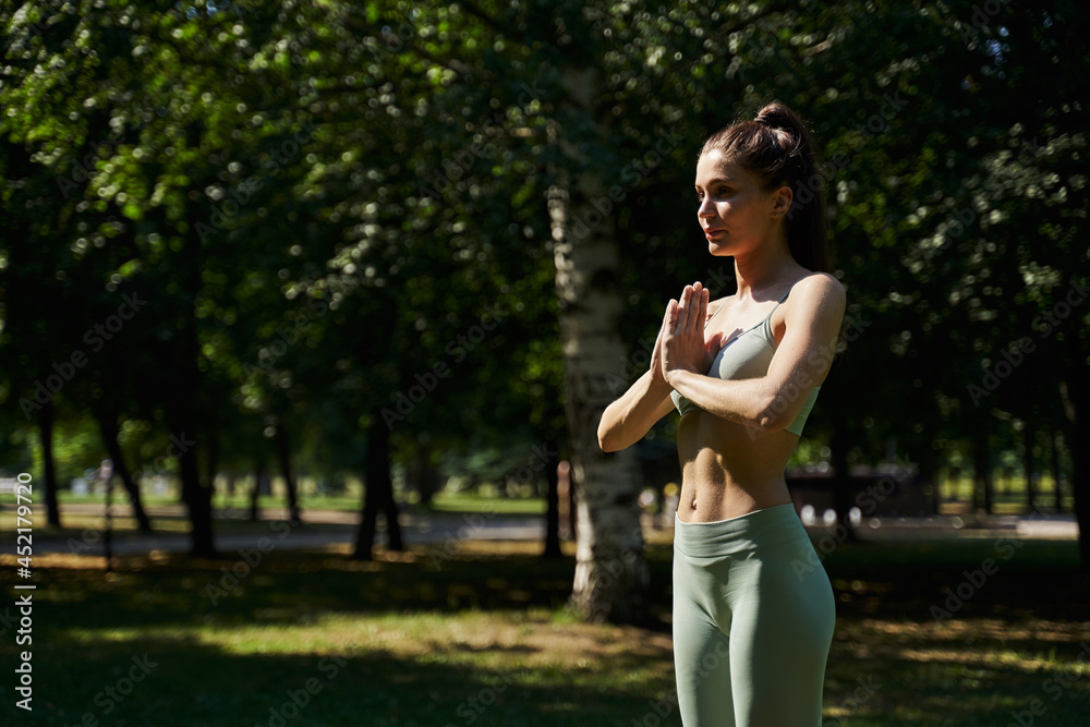 woman in the park doing yoga. pilates, gymnastics on the street in summer. sport exercises. young sports woman. arms folded meditation