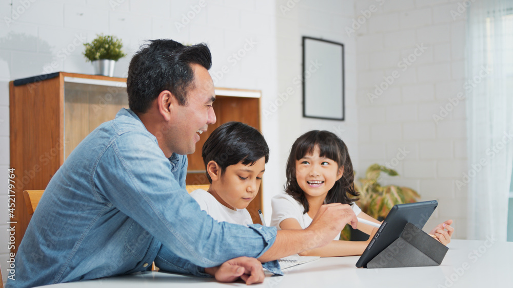 Asian father teach young son and daughter homework, using digital tablet at home. E-learning lifestyle, happy family homeschooling, children remote distance education, or internet technology concept Asian father teach young son and daughter homework, using digital tablet at home. E-learning lifestyle, happy family homeschooling, children remote distance education, or internet technology concept