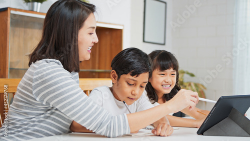 Asian mother teach young son and daughter homework, using digital tablet at home. E-learning lifestyle, family homeschooling, children remote distance education, or internet technology